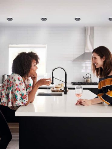 Three friends laughing together while cooking in a bright kitchen.