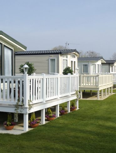 Modern mobile home with porch and fenced yard, ready for sale.